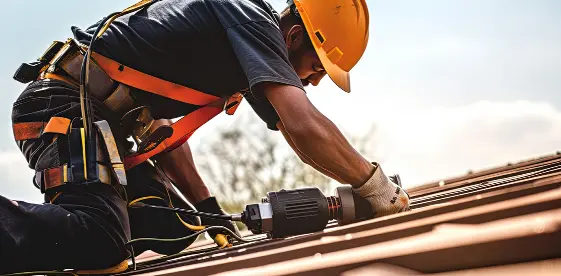A roofer on a house installing shingles with a nail gun